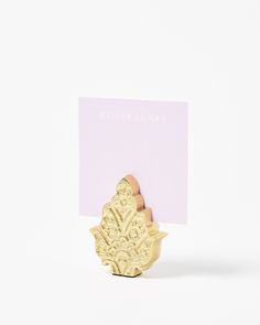 a gold brooch sitting on top of a white table next to a pink card