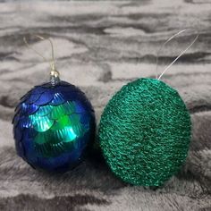 two green and blue ornaments sitting on top of a gray blanket next to each other