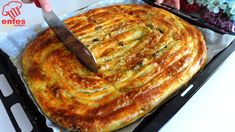 a person cutting into a large pizza on top of a pan with a knife in it