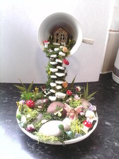 a white plate topped with lots of rocks and plants next to a cup filled with candles