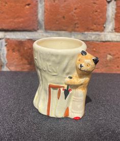 a ceramic cup with a bear on it sitting in front of a brick wall,