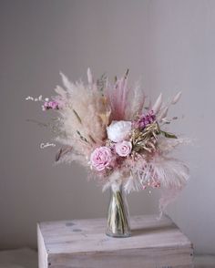 a vase filled with flowers and feathers on top of a wooden box