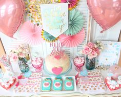 a table topped with pink and blue desserts next to heart shaped balloons on top of a wall