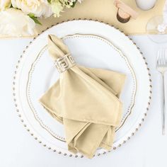 a white plate topped with a napkin and silverware next to a flower vase on top of a table