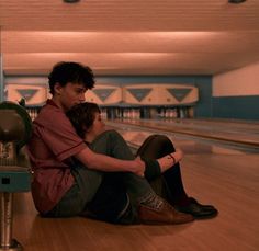 two young men sitting on the floor in a bowling alley with their arms around each other