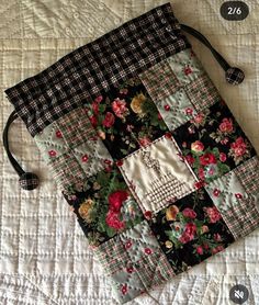 a quilted bag sitting on top of a white bed covered in black and red flowers