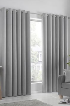 a living room with grey curtains and a gray chair in front of a window that has a white rug on the floor