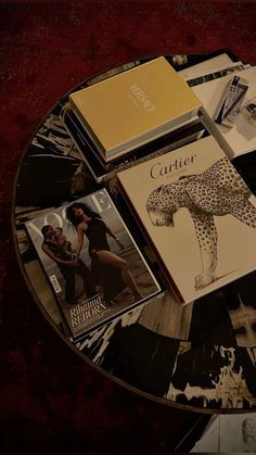 magazines and books are arranged on a round glass coffee table with red velvet flooring