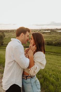 a man and woman standing next to each other on a dirt road in the middle of a field