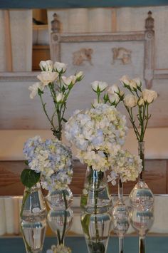 three vases filled with white and blue flowers on top of a glass table next to a mirror