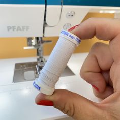 a person is sewing on a machine with their hand holding the needle and thread in front of them