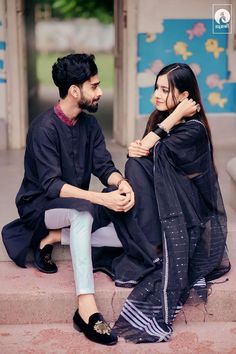 a man sitting next to a woman on top of a cement step in front of a building