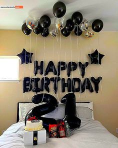 a birthday party with balloons and gifts on the bed in front of a happy birthday sign