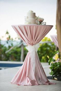 a wedding cake on top of a table with pink draping and ribbon around it