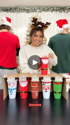 a group of people standing around each other with cups in front of them and santa hats on their heads