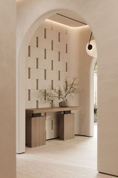 an archway leading into a room with white walls and flooring, along with two planters on either side of the table