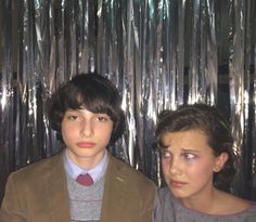 two young boys standing next to each other in front of tinsel foil curtain backdrop