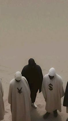 several people in white and black robes are standing on the sand with their backs to each other