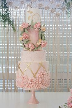 a three tiered cake with pink flowers on top and gold trimmings around the edges