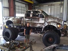 a man standing next to a large truck in a garage with lots of work on it