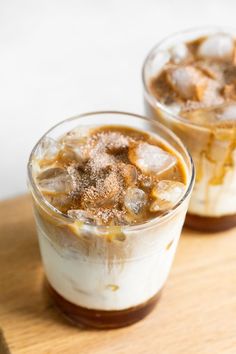 two glasses filled with ice and some food on top of a wooden table next to each other