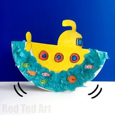 a paper plate shaped like a yellow submarine with fish and bubbles on the bottom, sitting in front of a blue background