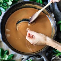 a person stirring something in a pot with a wooden spoon and green leaves around it