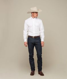 a man in a white shirt and cowboy hat is posing for a photo with his hands in his pockets