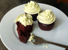 three cupcakes with white frosting on a plate next to a knife and fork