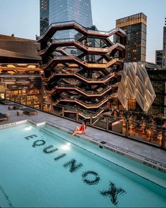 a woman sitting on the edge of a swimming pool in front of a cityscape