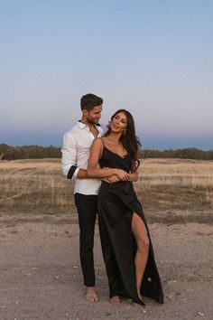 a man standing next to a woman on top of a dirt field in front of a blue sky