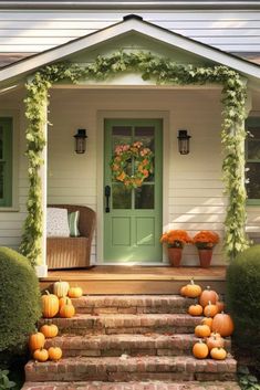 the front porch is decorated with pumpkins and greenery