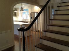 a staircase leading to an open kitchen and living room with white walls, hardwood flooring and stainless steel handrails