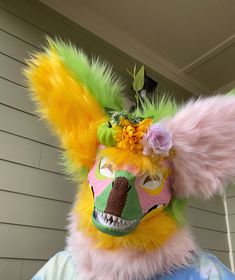 a person wearing a colorful mask with flowers on it's head and hair in the shape of a fox