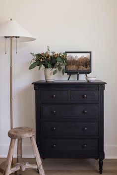 a black dresser with a potted plant on top and a white lamp next to it