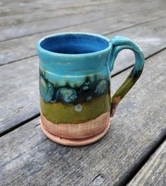 These coffee mugs are hand thrown on the wheel, then glazed with multiple glazes. The glaze pattern emulates   the landscape of the woods we live in. The bottom quarter of the mug is left unglazed, it is stained with iron oxide, then comes an olive green with mottled darker green and light colored flecks, topped by a sky blue. The inside is a darker blue. The mugs are about 4" tall, 3 1/4" wide on the bottom, 3" across on the top. They hold 12 oz of your favorite hot beverage. They are dishwasher safe. All glazes that I use are food safe. A Sky, Iron Oxide, Hand Thrown, The Landscape, Food Safe, Hot Drink, Sky Blue, Dark Green