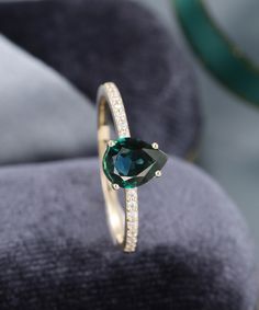 a ring with a green stone and diamond set in the center on a velvet cushion