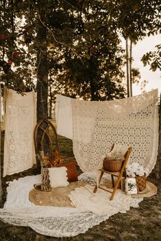 an old fashioned chair sitting on top of a blanket next to a wooden chair under a tree