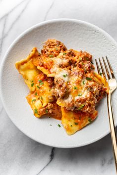 a white plate topped with lasagna covered in meat and cheese next to a fork