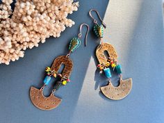 Add a touch of bohemian flair to your jewelry collection with these stunning handcrafted dangle earrings. Each pair is meticulously designed using a unique combination of raw brass, blue apatite beads, Czech glass beads, and striped seed beads. The raw brass components have been carefully hammered and hand-stamped with tiny stars, creating a fun and unique texture which is highlighted with a patina finish. The blue apatite beads bring a vibrant pop of color, while the Czech glass beads and striped seed beads add intricate detail and depth. At 4 1/8" long, these earrings make a bold statement, perfect for those who love to stand out. Their rustic feel and bohemian style make them versatile enough to complement both casual and dressy outfits. -Handcrafted just for you in my Brooklyn studio! Artisan Nickel Free Beaded Earrings For Festivals, Bohemian Beaded Dangling Earrings, Bohemian Beaded Dangle Earrings, Colorful Beaded Brass Dangle Earrings, Beaded Bohemian Chandelier Earrings, Bohemian Beaded Chandelier Earrings, Artsy Jewelry With Dangling Round Beads, Handmade Bohemian Copper Earrings, Bohemian Beaded Earrings With Colorful Beads