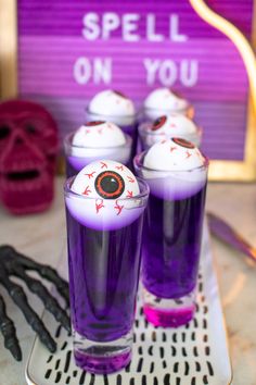 three glasses filled with purple liquid and spooky eyes on the top, sitting on a tray