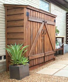 a wooden storage shed sitting on top of a patio next to a planter filled with flowers