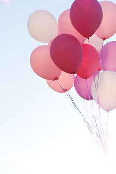 a bunch of pink and white balloons floating in the air on a clear blue day