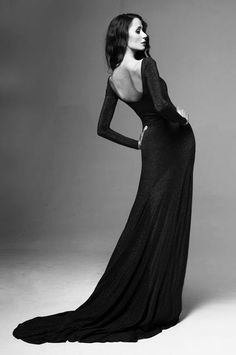 a woman in a long black dress posing for a magazine cover shoot with her back to the camera