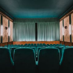 an empty theater with rows of blue seats in front of a curtained wall and windows