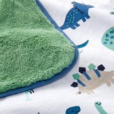 a green and blue dinosaur blanket laying on top of a bed