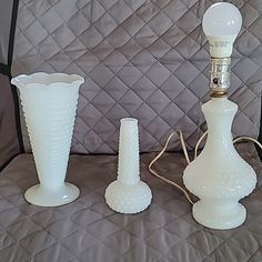 three white vases sitting on top of a bed next to a light bulb and cord