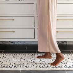 a woman standing on a rug in front of a white cabinet with drawers and cabinets