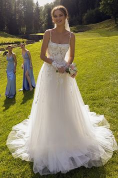 a woman in a wedding dress standing on the grass with two other women behind her