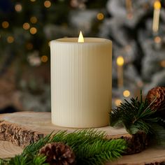 a white candle sitting on top of a wooden table next to pine cones and evergreen branches